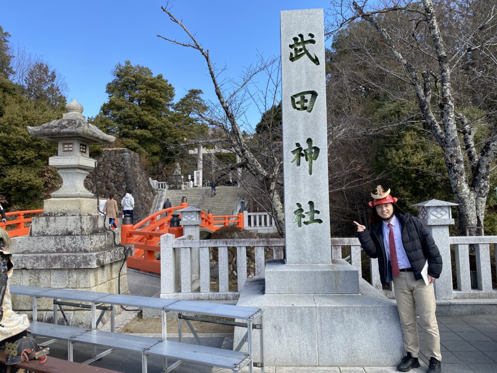「武田神社」碑の前で記念撮影（奥には水堀や土塁の跡がある）